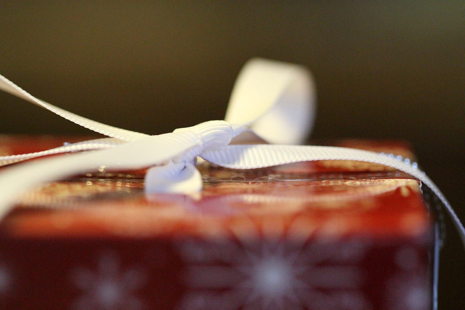 Nahaufnahme eines Geschenks in rotem Papier mit Schneeflockenmuster und weißer Ripsbandschleife vor dunklem Hintergrund