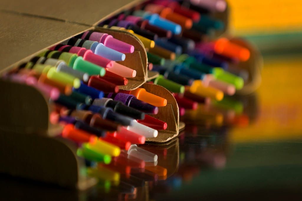 Viele bunte Wachsmalstifte in Pink, Gelb, Grün, Blau und Orange in einer Pappschachtel